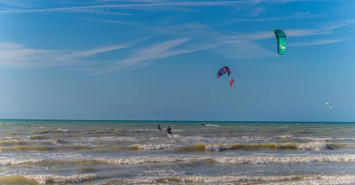 Scène de kitesurf passionnante par une journée ensoleillée avec des cerfs-volants colorés flottant au-dessus des vagues de l'océan.