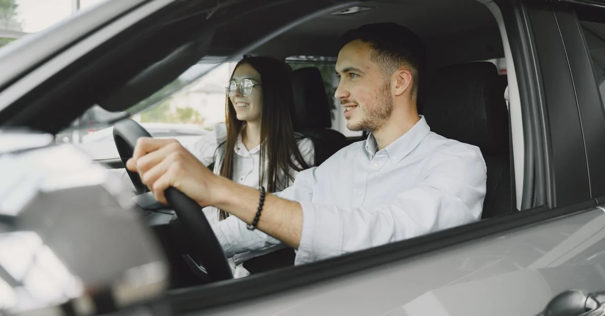 Un jeune couple souriant en conduisant ensemble dans l'intérieur d'une voiture moderne.