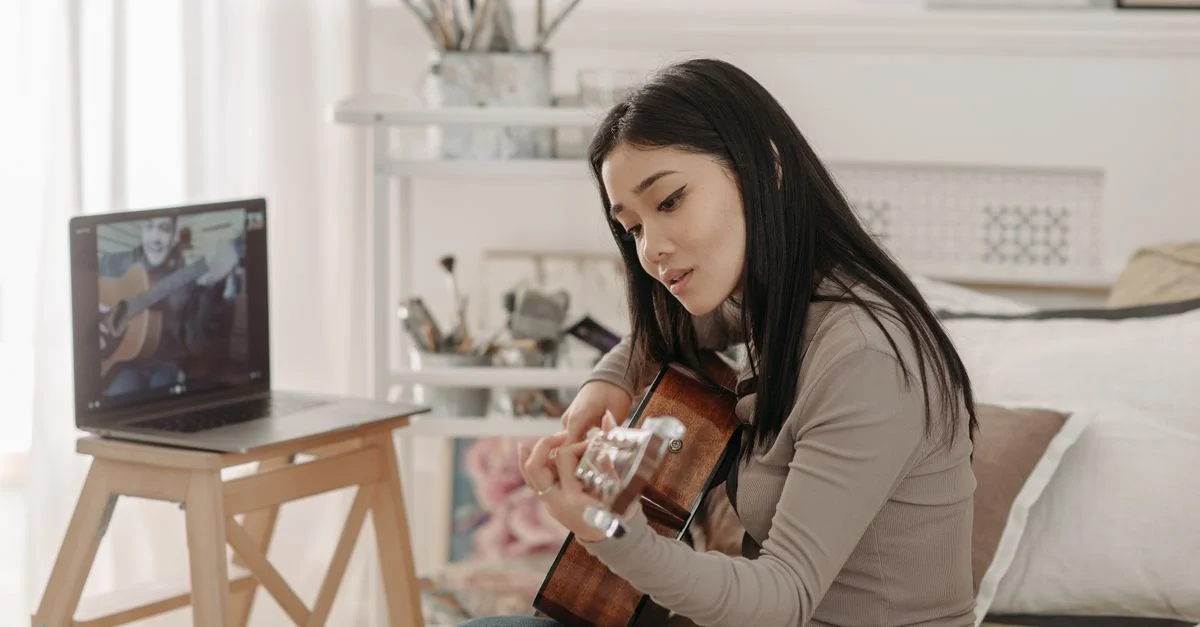 Femme asiatique suivant un cours de guitare en ligne à domicile avec un ordinateur portable.