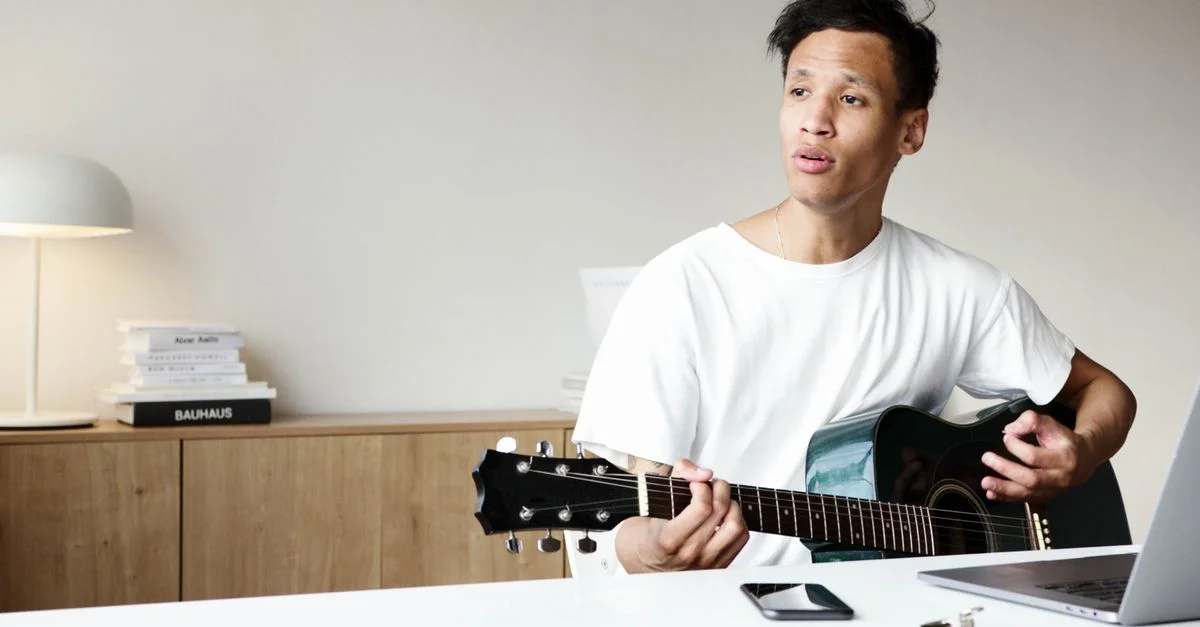 Un jeune homme joue de la guitare acoustique à l'intérieur, dégagent passion et créativité musicale.