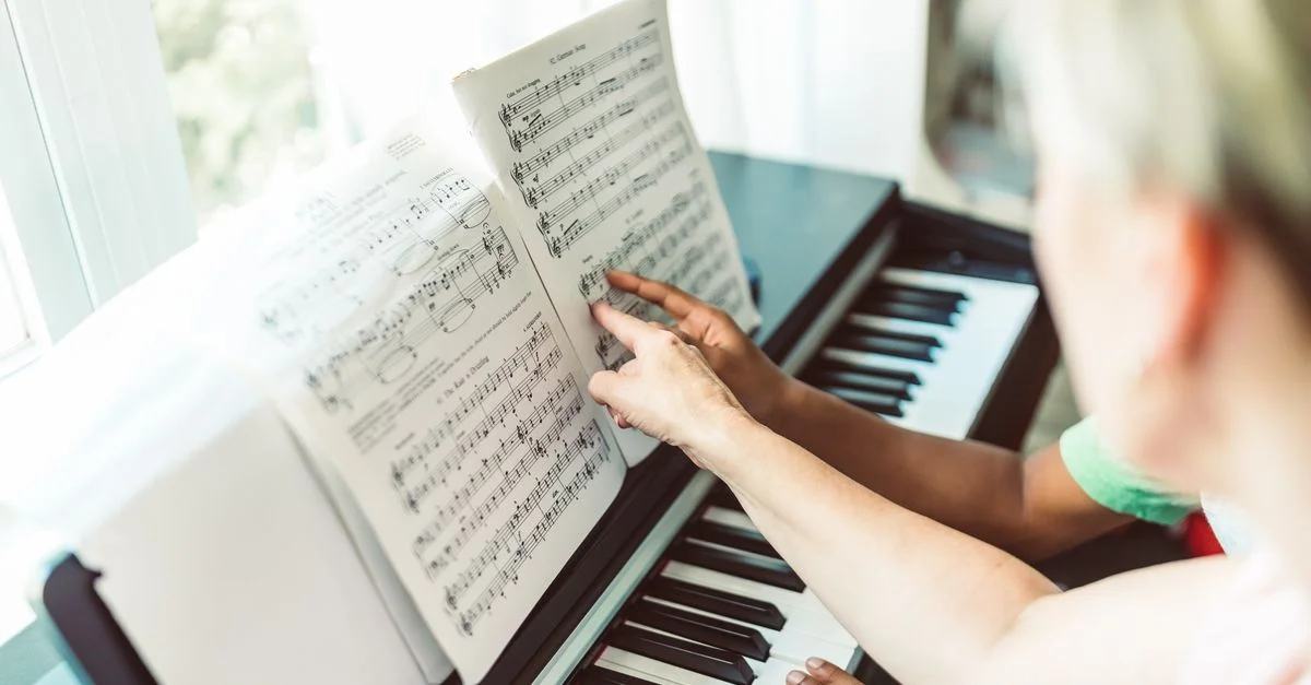 Un enfant apprend le piano auprès d'un professeur adulte avec des partitions visibles.