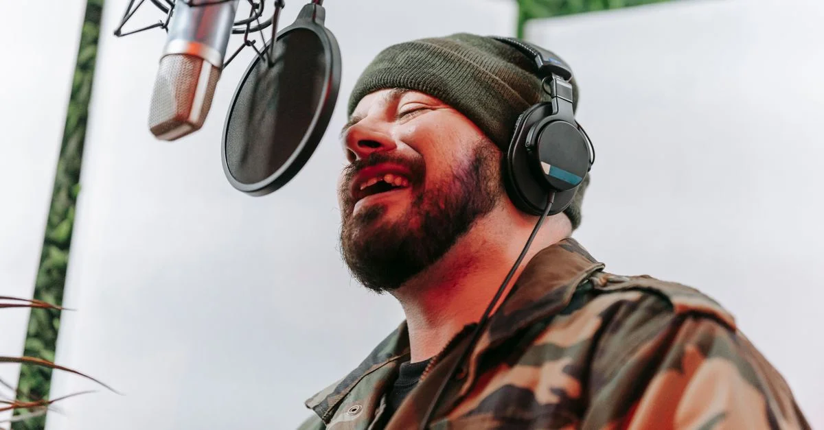 Homme barbu chantant avec passion dans un studio de musique avec des écouteurs et un microphone.
