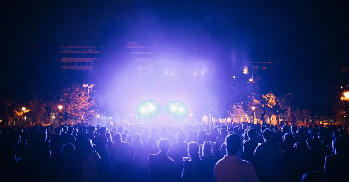 Une scène de concert vivante en plein air la nuit avec des lumières colorées et un large public.
